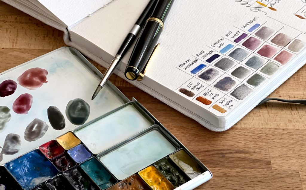 An open sketchbook showing neutral and violet color mixes.