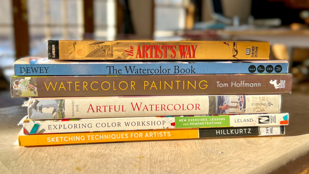 A stack of art books in the sun next to a couch.